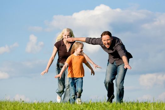 Happy family (mother, father and kid) having a walk in the nature playing tag