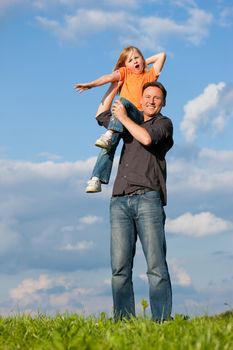 Father and his kid - daughter - playing together at a meadow, he is carrying her on his shoulders