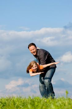 Father and his kid - daughter - playing together at a meadow, he is carrying her on his hands