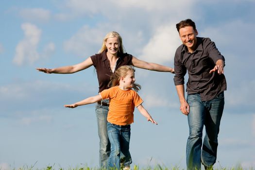 Happy family (mother, father and kid) having a walk in the nature playing tag