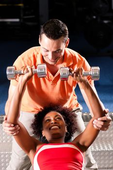 Woman with her personal fitness trainer in the gym exercising with dumbbells