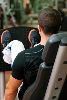 Man doing fitness training on leg press with weights in a gym