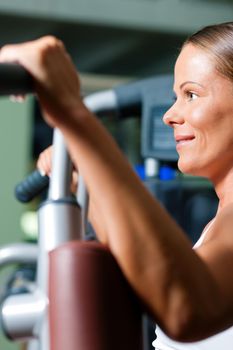 Woman doing fitness training on a butterfly machine with weights in a gym