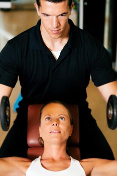 Woman with her personal fitness trainer in the gym exercising with dumbbells