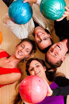 Group of four friends lying in a bowling alley having fun, holding their bowling balls above them