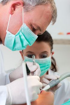 Female patient with dentist and assistant in a dental treatment, wearing masks and gloves, Dentist and assistant bowing over her using sucker and drill