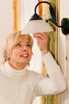 Woman changing a light bulb in a lamp hanging in her apartment