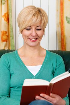 Mature woman is reading a book at home in her living room