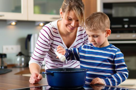 Family cooking in their kitchen - the son is putting salt into the boiling water