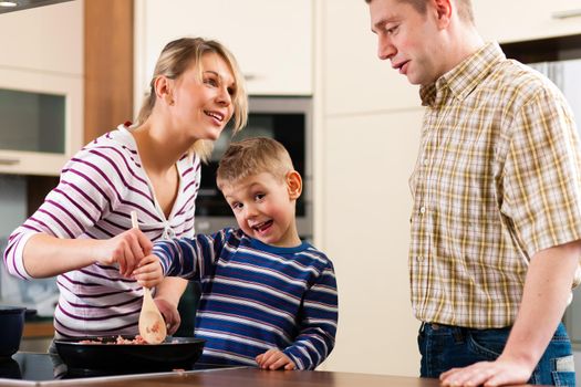 Family cooking in their kitchen - mother making some spaghetti sauce, son is stirring and daddy looking