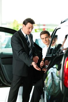 Man buying a car in dealership sitting in his new auto, the salesman talking to him and explaining details