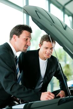 Man buying a car in dealership looking under the hood at the engine