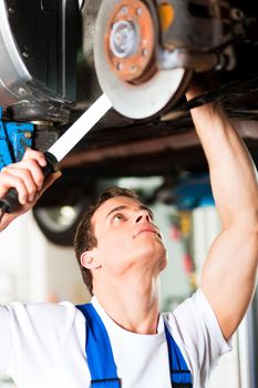 Auto mechanic in his workshop looking under a car on a hoist