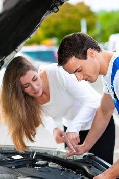 Woman talking to a car mechanic in a parking area, both are standing next to the car