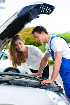 Woman talking to a car mechanic in a parking area, both are standing next to the car
