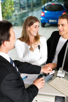 Sales situation in a car dealership, the young couple buys a new car from an agent and pays with credit card