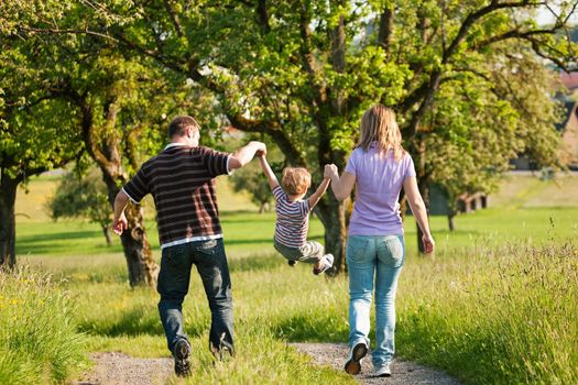Family having a walk outdoors in summer, throwing their little son in the air in a playful way