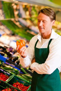 Shop assistant in a supermarket at the vegetable shelf inspecting the stuff for sale