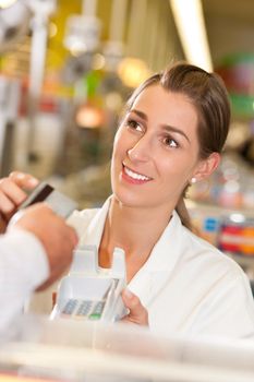 Male customer in supermarket handing his credit card to cashier at the checkout desk in order to pay