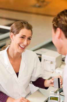 Male customer in supermarket handing his credit card to cashier at the checkout desk in order to pay