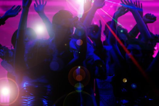 Silhouettes of dancing people having a celebration in a disco club, the light show is sending laser beams through the backlit scene