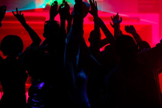 Silhouettes of dancing people having a celebration in a disco club, the light show is sending laser beams through the backlit scene