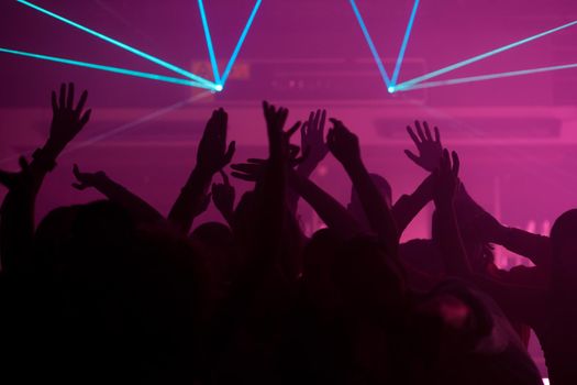 Silhouettes of dancing people having a celebration in a disco club, the light show is sending laser beams through the backlit scene