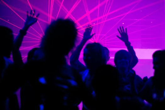 Silhouettes of dancing people having a celebration in a disco club, the light show is sending laser beams through the backlit scene, FOCUS IN ON THE BEAMS!