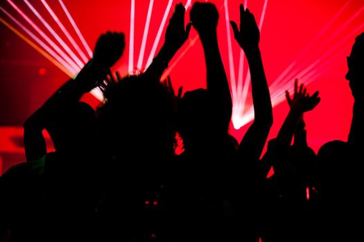 Silhouettes of dancing people having a celebration in a disco club, the light show is sending laser beams through the backlit scen