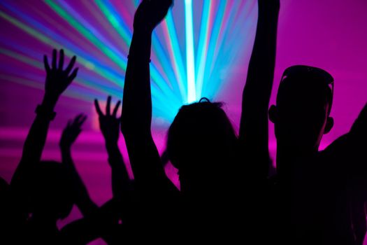 Silhouettes of dancing people having a celebration in a disco club, the light show is sending laser beams through the backlit scene