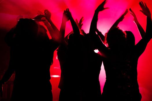 Silhouettes of dancing people having a celebration in a disco club, light is shining through the silhouettes of people