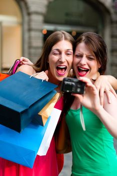 Two woman being friends shopping downtown with colourful shopping bags and taking a picture from themselves