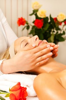 Woman enjoying a wellness head massage in a spa setting with roses in the background, she is very relaxed