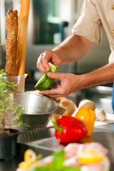 Close up of chef in a commercial restaurant kitchen working; he is preparing vegetables