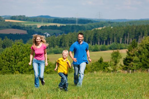 Young family having fun in the sun running over the meadow an a bright summer day