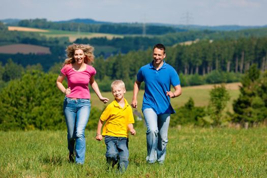 Young family having fun in the sun running over the meadow an a bright summer day