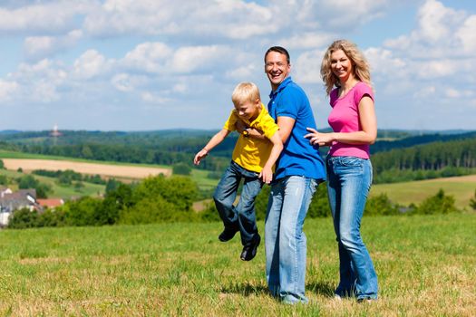 Young family having a walk in the sun over the meadow on a bright summer day and making jokes