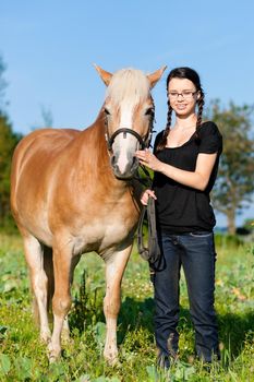 Teenage girl standing on a meadow in summer with her horse