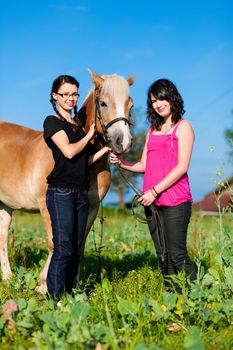 Teenage girls standing on a meadow in summer with their horse