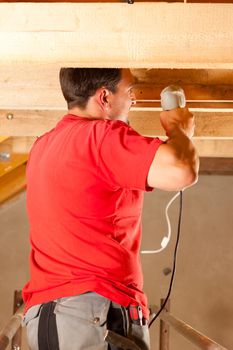Carpenter or construction worker with hand drill working in the roof framework inside a house