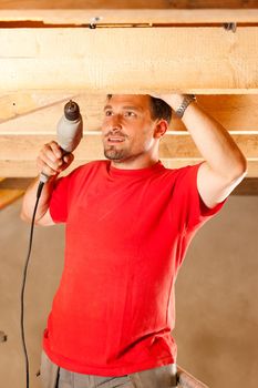 Carpenter or construction worker with hand drill working in the roof framework inside a house