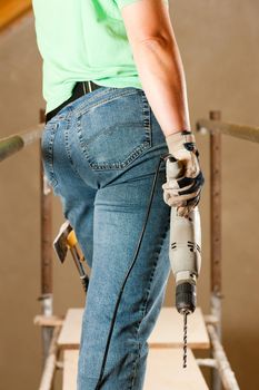 Female construction worker with hand drill standing on a scaffold