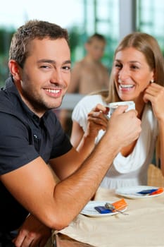 Young couple - man and woman - drinking coffee in a cafe in front of a glass facade