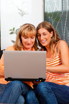 Daughter explaining internet to her mother at home, both women are sitting in front of a laptop PC