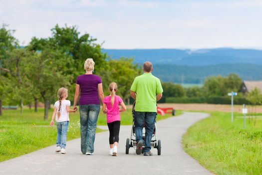 Family with three children (one baby lying in a baby buggy) walking down a path outdoors, two kids are running ahead, there is also a dog