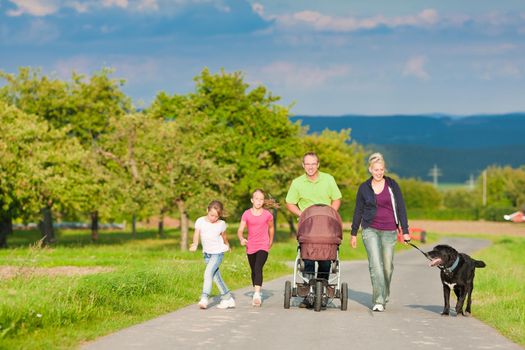 Family with three children (one baby lying in a baby buggy) walking down a path outdoors, there is also a dog