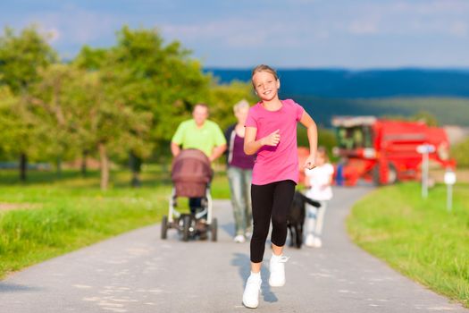 Family with three children, one baby lying in a baby buggy, walking down a path outdoors, two kids are running ahead, there is also a dog