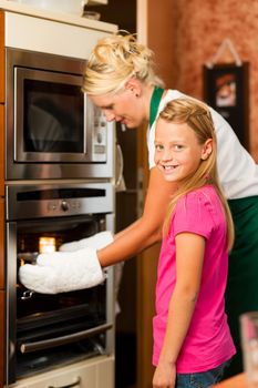 Mother and daughter cooking - they are putting roast in the oven