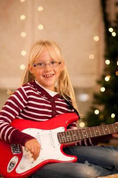 Young child with her guitar - presumably a present - in front of a Christmas tree