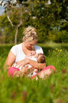 Mother breastfeeding her baby on a great sunny day in a meadow with lots of green grass and wild flowers